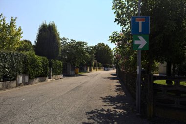 Güneşli bir günde İtalyan köyünün duvarlarında çitlerle ve bahçelerle çevrili bir sokak.