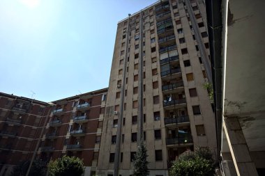 Güneşli bir günde, bir İtalyan kasabasının yerleşim bölgesinde park halindeki arabalarla apartman dairesi arasında.