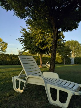Gün batımında bir bahçede, ağaçların yanındaki iskemleler.
