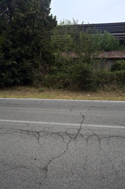 İtalya kırsalındaki terk edilmiş fabrika ağaçlarla çevrili ve yağmurdan önce bulutlu bir günde yolun karşı tarafından görülüyor.