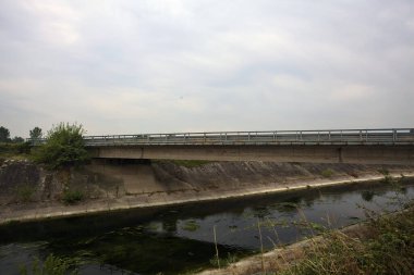 Yağmur yağmadan önce bulutlu bir günde İtalya kırsalında bir eğlence kanalı üzerinde köprü