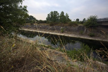 Yağmur yağmadan önce bulutlu bir günde İtalya kırsalında bir eğlence kanalı üzerinde köprü