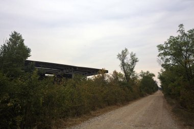 İtalya 'da yağmur yağmadan önce bulutlu bir günde terk edilmiş bir fabrikanın yanındaki ağaçlarla çevrili toprak yol.