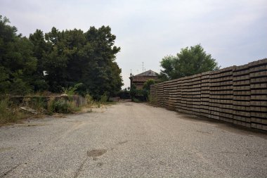 Bulutlu bir günde ağaçlarla çevrili bir grup ev ve kapıya açılan endüstriyel bir tesisin açıklıktaki çakıl yolu.