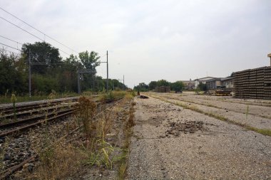 İtalya 'nın kırsal kesimlerinde bulutlu bir günde tren istasyonunun açıklığından görülen işlevsel bir demiryolunun yanında terk edilmiş raylar.