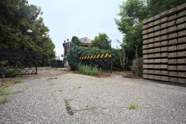 Bulutlu bir günde ağaçlarla çevrili bir grup ev ve kapıya açılan endüstriyel bir tesisin açıklıktaki çakıl yolu.