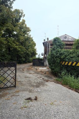 Bulutlu bir günde ağaçlarla çevrili bir grup ev ve kapıya açılan endüstriyel bir tesisin açıklıktaki çakıl yolu.