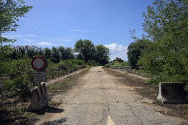 İtalya kırsalında güneşli bir günde beton bariyerlerle kapatılmış yıpranmış asfalt köprü