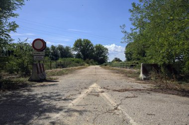 İtalya kırsalında güneşli bir günde beton bariyerlerle kapatılmış yıpranmış asfalt köprü