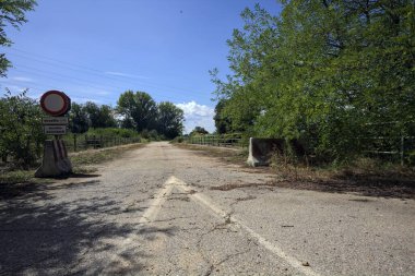 İtalya kırsalında güneşli bir günde beton bariyerlerle kapatılmış yıpranmış asfalt köprü