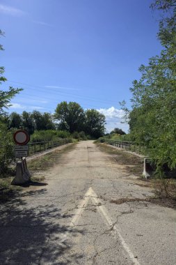 İtalya kırsalında güneşli bir günde beton bariyerlerle kapatılmış yıpranmış asfalt köprü