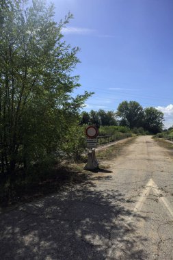 İtalya kırsalında güneşli bir günde beton bariyerlerle kapatılmış yıpranmış asfalt köprü