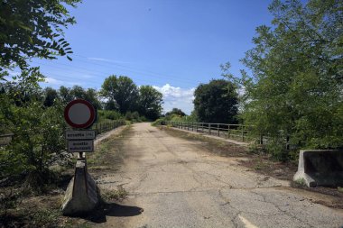 İtalya kırsalında güneşli bir günde beton bariyerlerle kapatılmış yıpranmış asfalt köprü
