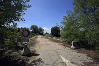 İtalya kırsalında güneşli bir günde beton bariyerlerle kapatılmış yıpranmış asfalt köprü
