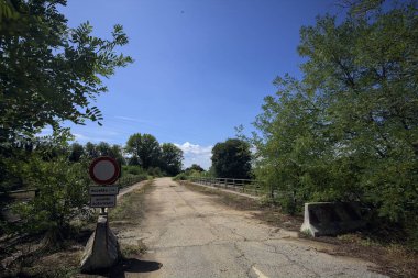 İtalya kırsalında güneşli bir günde beton bariyerlerle kapatılmış yıpranmış asfalt köprü