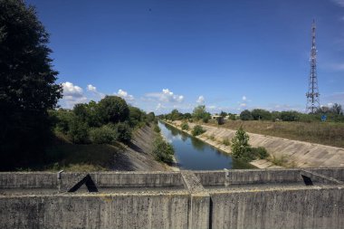 İtalya kırsalında güneşli bir günde ağaçlarla çevrili eğlence kanalı bir köprünün üstünden görülüyor.
