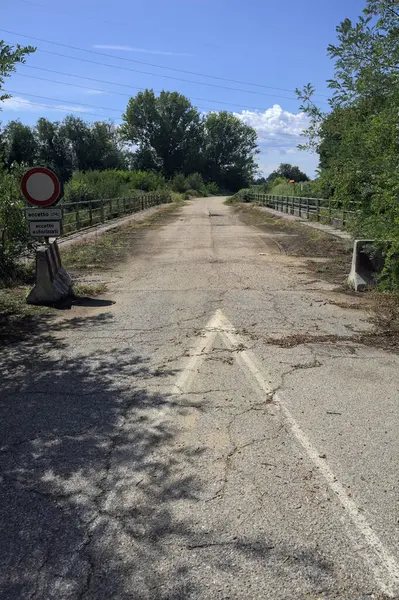 İtalya kırsalında güneşli bir günde beton bariyerlerle kapatılmış yıpranmış asfalt köprü