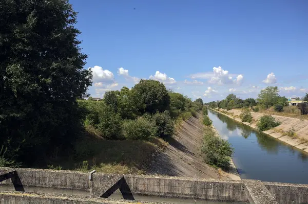 İtalya kırsalında güneşli bir günde ağaçlarla çevrili eğlence kanalı bir köprünün üstünden görülüyor.