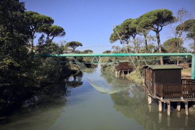 Güneşli bir günde, parktaki bir su deresinin kıyısında asılı ağlarla balıkçı kulübeleri.
