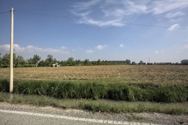 İtalya kırsalında güneşli bir günde ekili tarlaların yanında dar bir kır yolu.