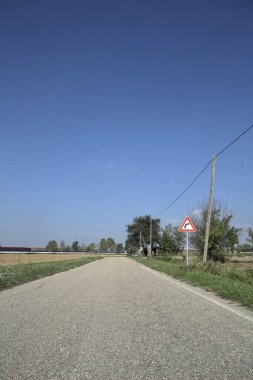 Güneşli bir günde kenarında bir tabela olan virajın yanındaki kır yolu.