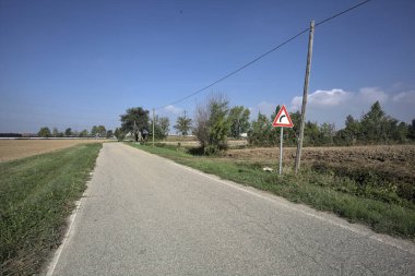 Güneşli bir günde kenarında bir tabela olan virajın yanındaki kır yolu.