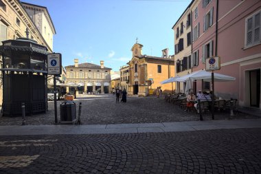 Küçük bir kilise ve bir restoranın masalarıyla süslü bir meydan.