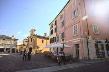Küçük bir kilise ve bir restoranın masalarıyla süslü bir meydan.