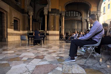 Seyirci izlerken, bir sarayın verandasında piyano çalan bir kadın.