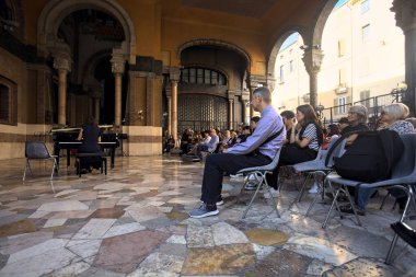 Seyirci izlerken, bir sarayın verandasında piyano çalan bir kadın.