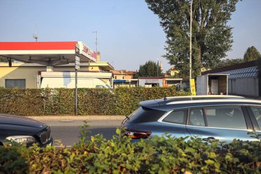 Köy yolundaki Esso benzin istasyonu. Gün batımında çalılığın arkasından görünen bir köy ve baca.