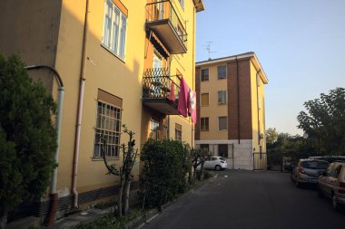 Gün batımında bir apartmanın yanında bitkilerle ve park edilmiş arabalarla çevrili bir sokak.