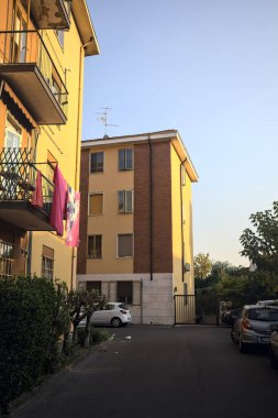 Gün batımında bir apartmanın yanında bitkilerle ve park edilmiş arabalarla çevrili bir sokak.