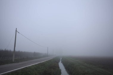 İtalya kırsalında sisli bir günde tarlaların yanında bir siper ve elektrik hattı ile çevrili bir yol.