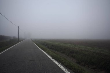 İtalya kırsalında sisli bir günde tarlaların yanında bir siper ve elektrik hattı ile çevrili bir yol.