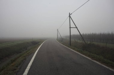 İtalya kırsalında sisli bir günde tarlaların yanında bir siper ve elektrik hattı ile çevrili bir yol.