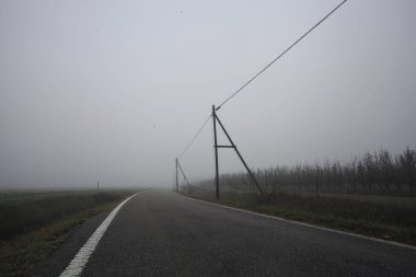 İtalya kırsalında sisli bir günde tarlaların yanında bir siper ve elektrik hattı ile çevrili bir yol.