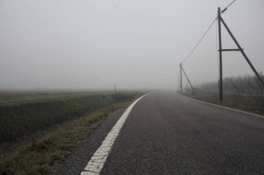 İtalya kırsalında sisli bir günde tarlaların yanında bir siper ve elektrik hattı ile çevrili bir yol.