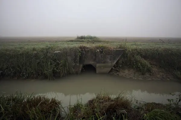 Drainage under a field going to a trench full of water on a foggy day in the italian countryside