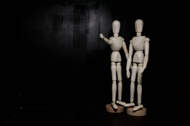 Siyah arka planda iki tahta heykel var. Biri kamerayı işaret ediyor.