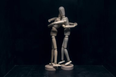 Siyah arka planda birbirine sarılan iki tahta heykel.