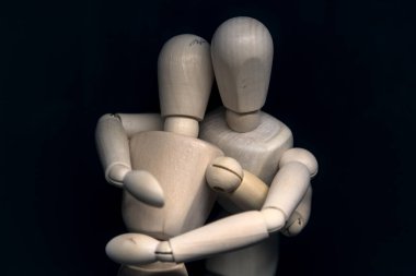 Siyah arka planda birbirine sarılan iki tahta heykel.