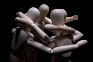 Siyah arka planda birbirine sarılan dört tahta heykel.