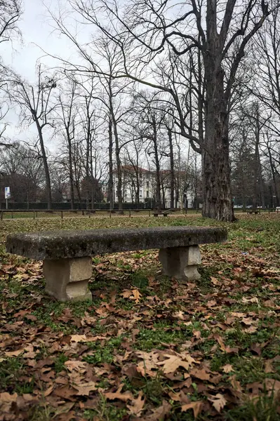 Stone bench in a lawn of a park on a cloudy day in autumn