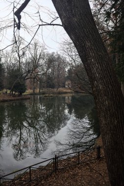 Kıyısında neoklasik bir tapınağı olan bir parkta gölet ve sonbaharda bulutlu bir günde ağaçların yansıması.