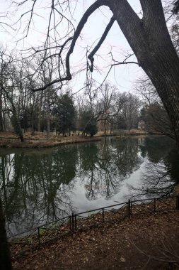 Kıyısında neoklasik bir tapınağı olan bir parkta gölet ve sonbaharda bulutlu bir günde ağaçların yansıması.