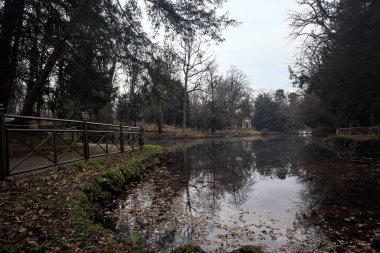 Kıyısında neoklasik bir tapınağı olan bir parkta gölet ve sonbaharda bulutlu bir günde ağaçların yansıması.