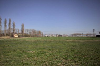 Yanı başında ağaçlar ve ufukta İtalya kırsalında bir köşk olan boş bir çayır.
