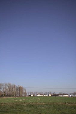 Yanı başında ağaçlar ve ufukta İtalya kırsalında bir köşk olan boş bir çayır.