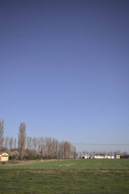 Yanı başında ağaçlar ve ufukta İtalya kırsalında bir köşk olan boş bir çayır.